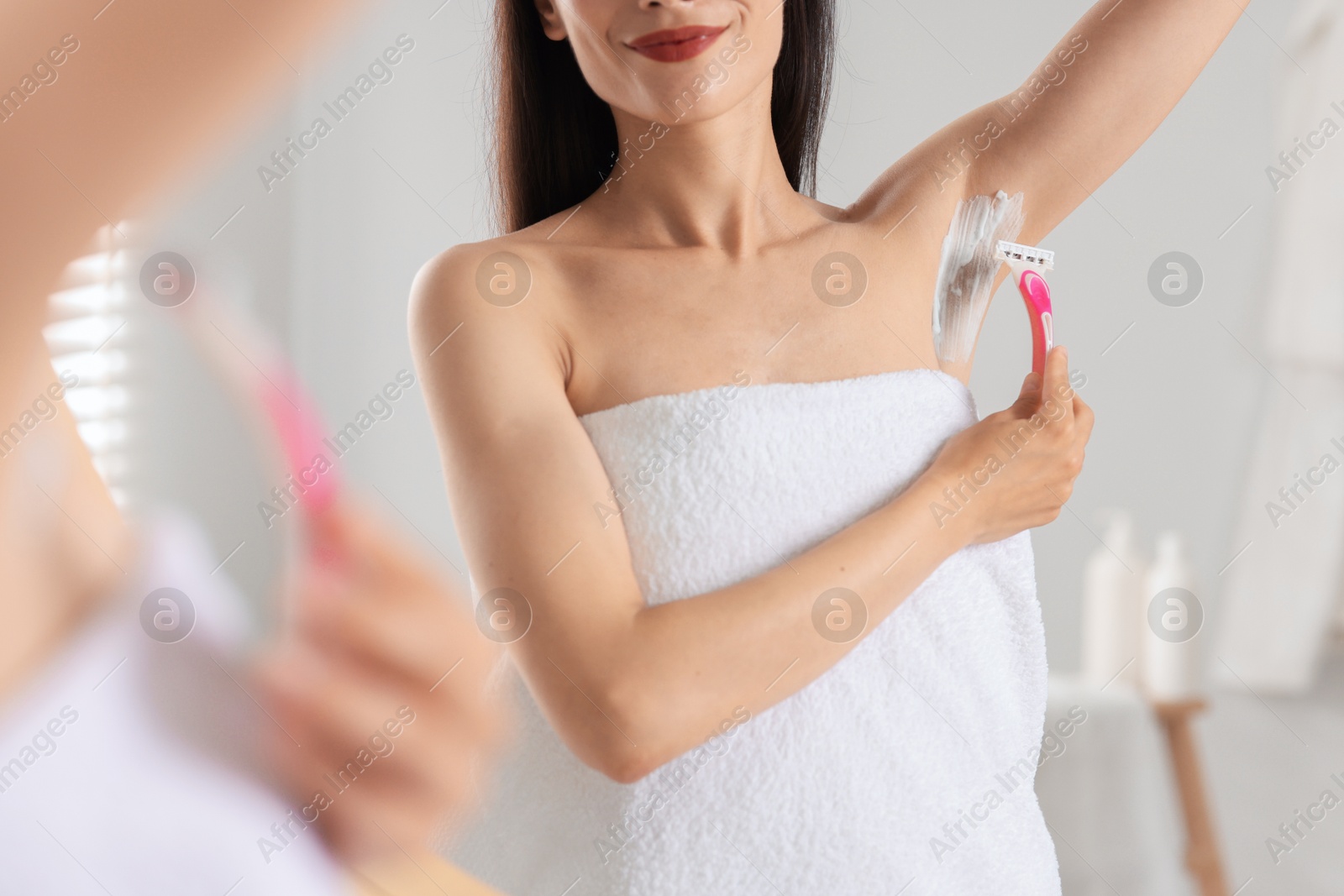 Photo of Woman shaving armpit near mirror indoors, closeup