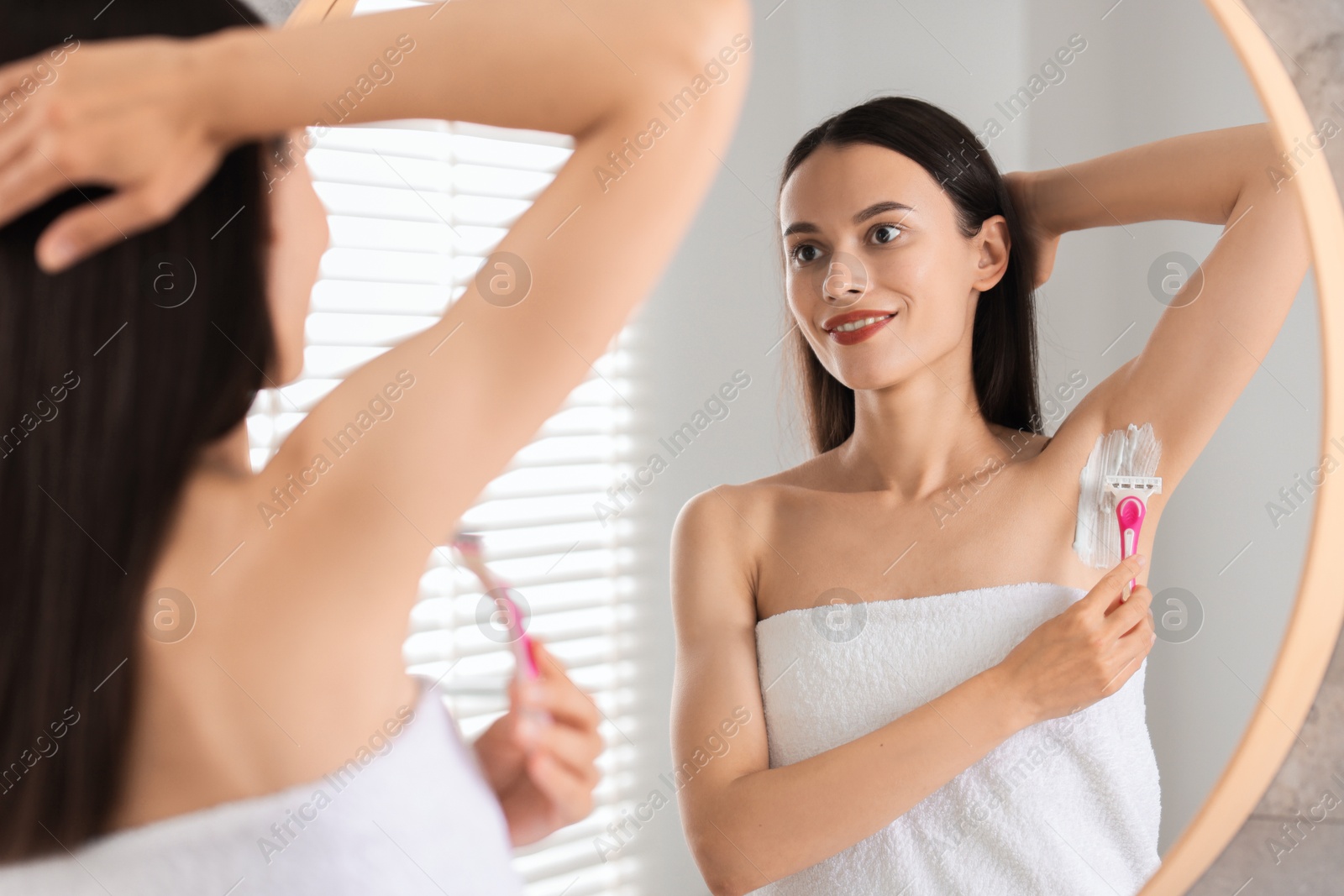 Photo of Smiling woman shaving armpit near mirror indoors, selective focus