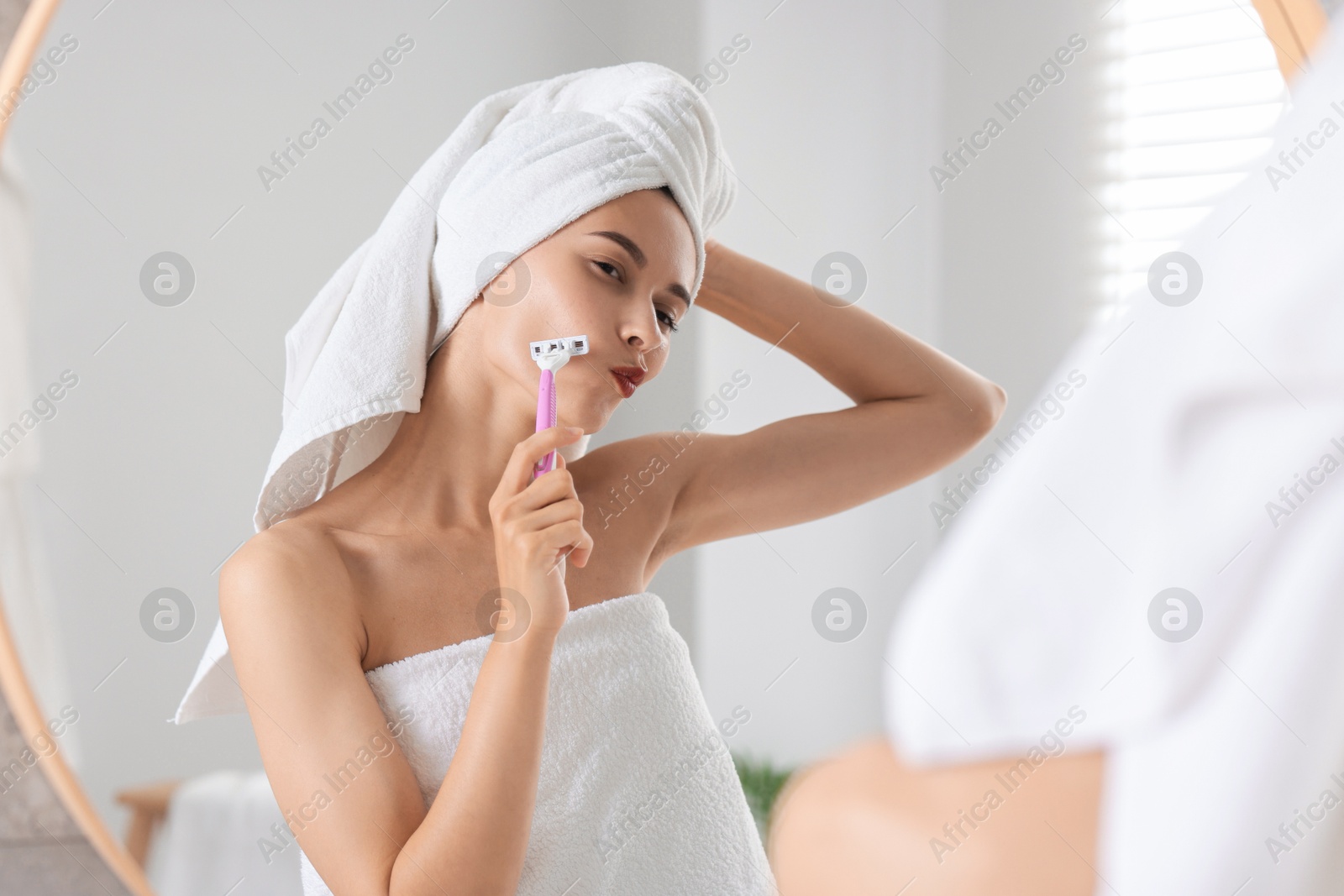 Photo of Beautiful woman shaving face near mirror indoors