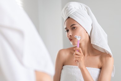 Photo of Beautiful woman shaving face near mirror indoors