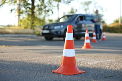 Photo of Examiner instructing student before exam at driving school test track, focus on traffic cone