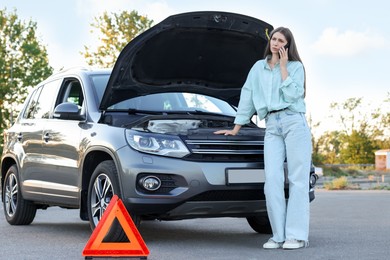 Stressed woman talking on phone near broken car outdoors