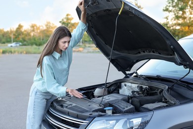 Photo of Stressed woman looking under hood of broken car outdoors