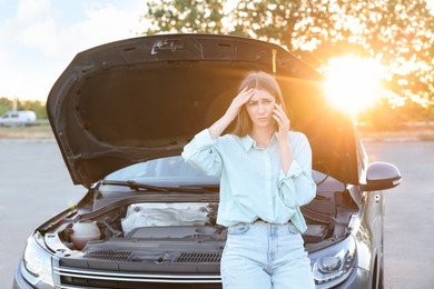 Stressed woman talking on phone near broken car outdoors