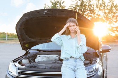 Photo of Stressed woman talking on phone near broken car outdoors