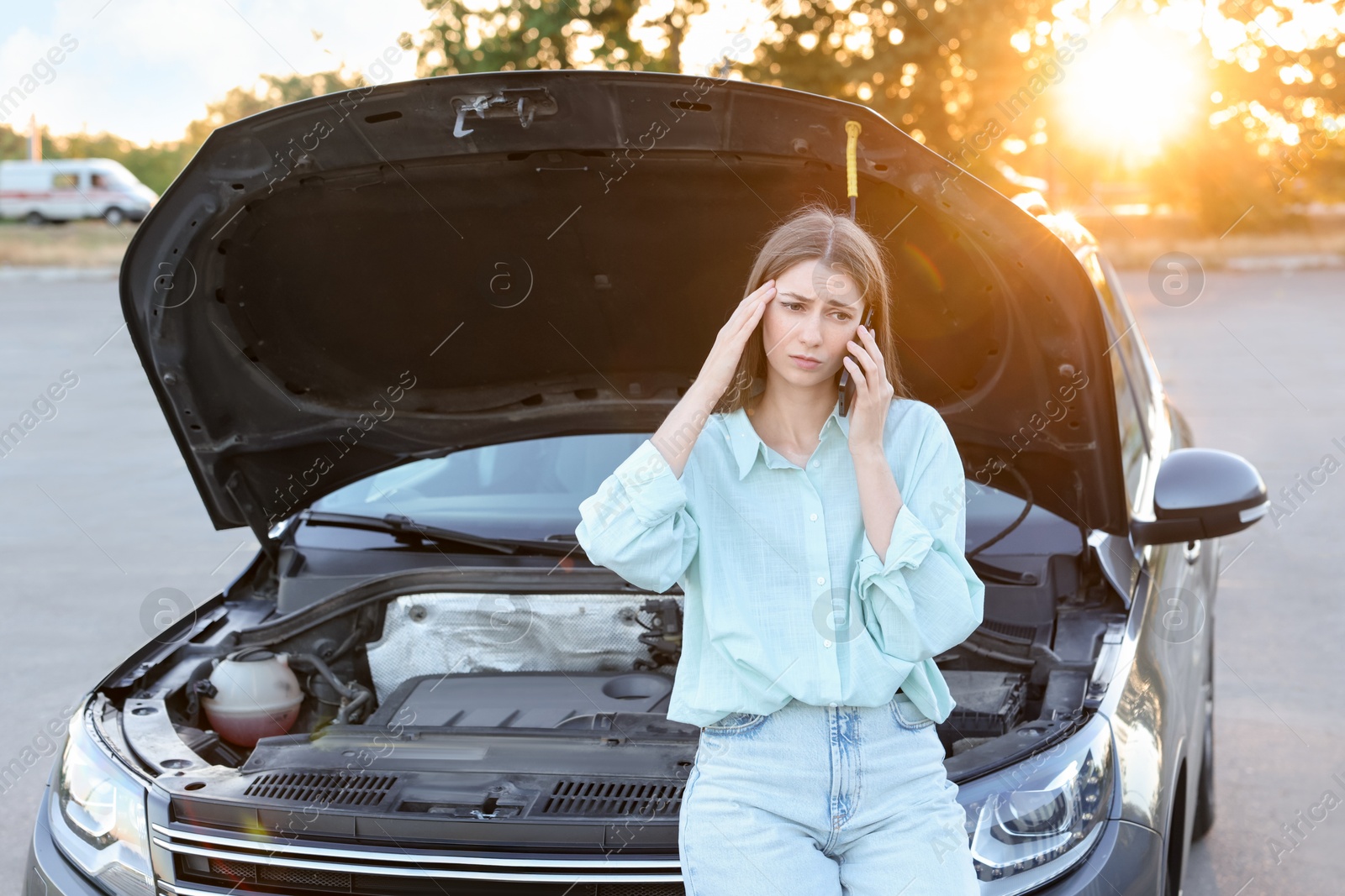 Photo of Stressed woman talking on phone near broken car outdoors