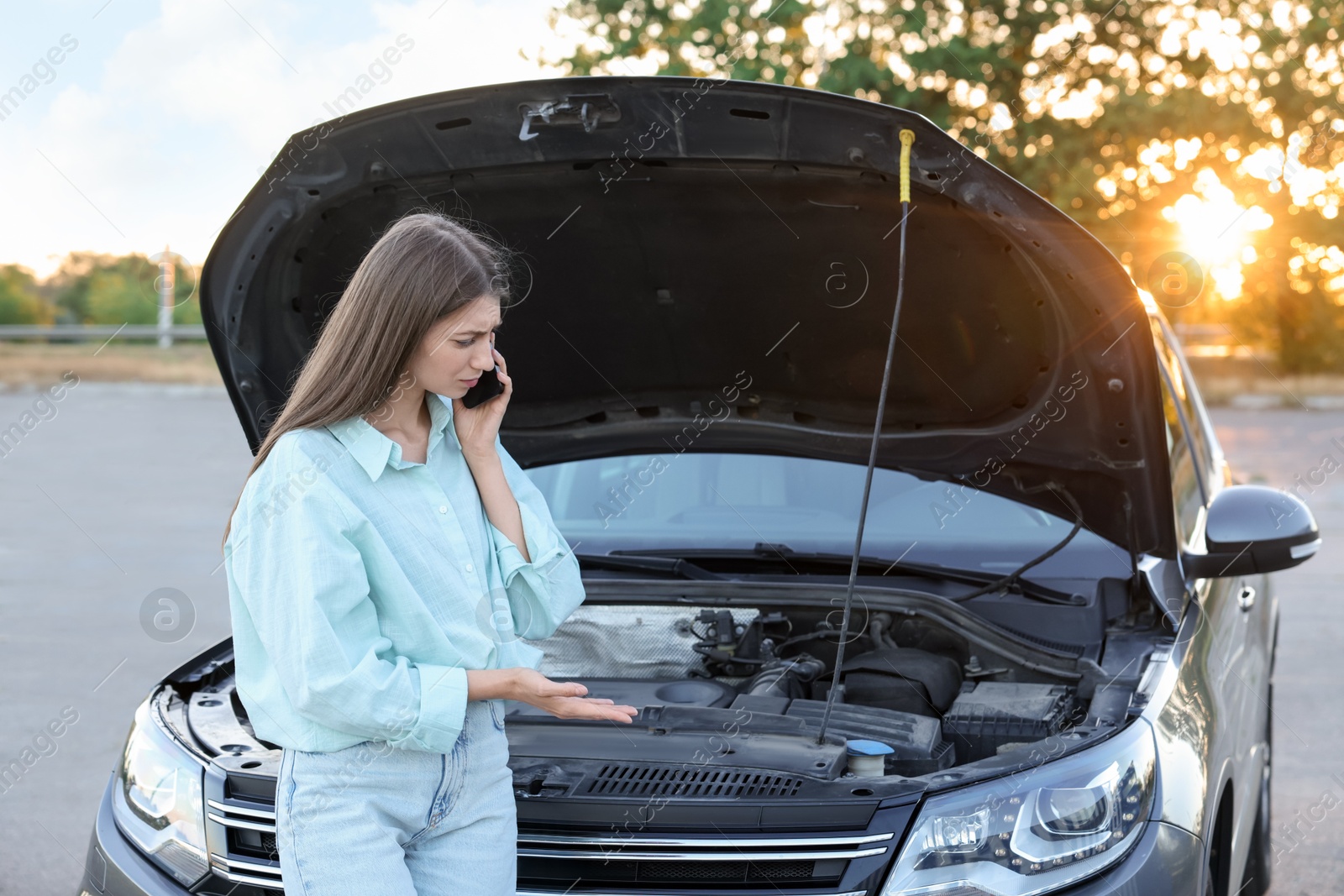 Photo of Stressed woman talking on phone near broken car outdoors