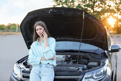 Photo of Stressed woman talking on phone near broken car outdoors