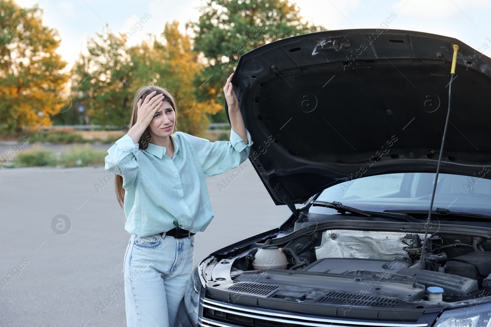 Photo of Stressed woman standing near broken car outdoors