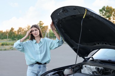 Stressed woman standing near broken car outdoors