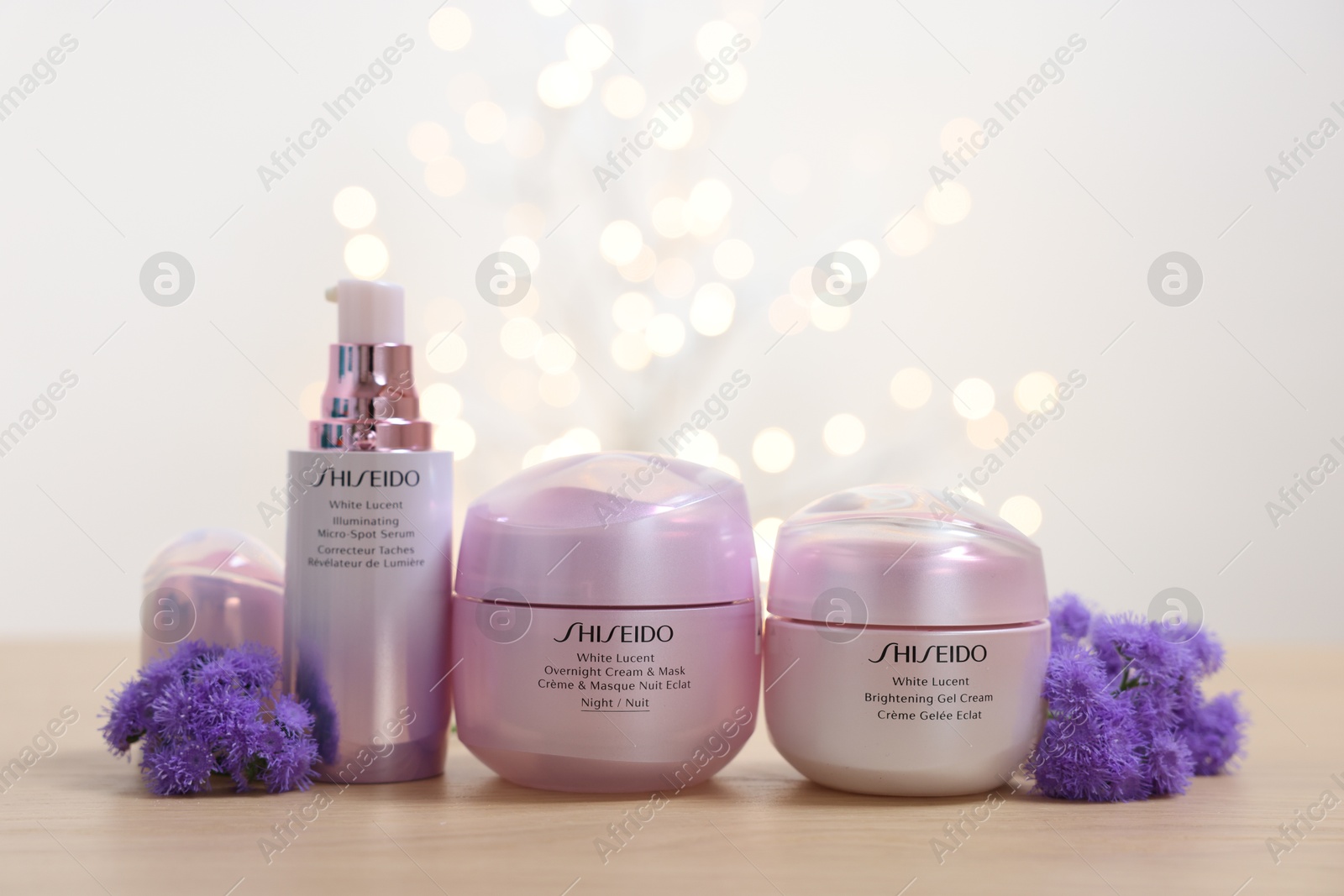 Photo of Leiden, Netherlands - June 11, 2024: Shiseido care cosmetic products and ageratum flowers on wooden table against light background with blurred lights