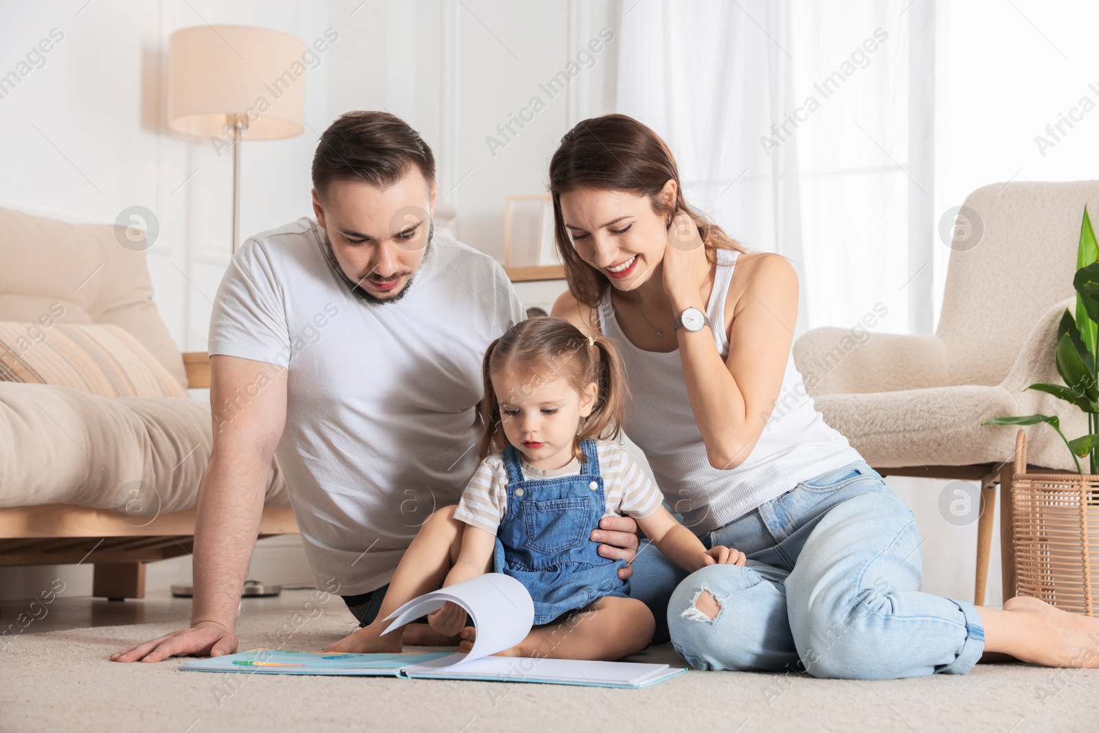 Photo of Happy family. Parents and their cute little daughter reading book at home