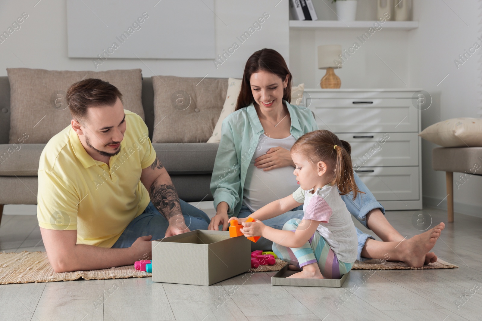 Photo of Happy family. Pregnant woman, her husband and cute little daughter playing with construction set at home