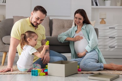 Photo of Happy family. Pregnant woman, her husband and cute little daughter playing with construction set at home