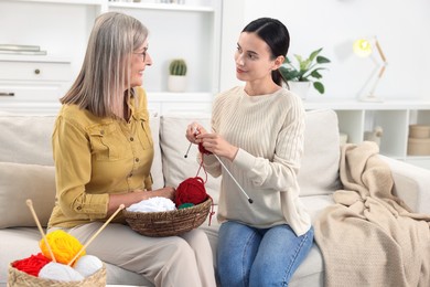 Photo of Smiling mother and daughter with skeins of yarn spending time together at home