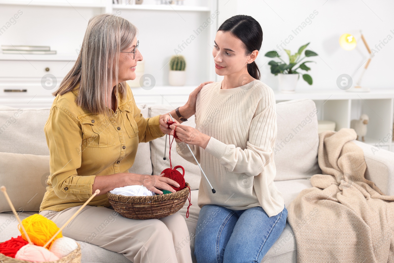 Photo of Smiling mother and daughter with skeins of yarn spending time together at home