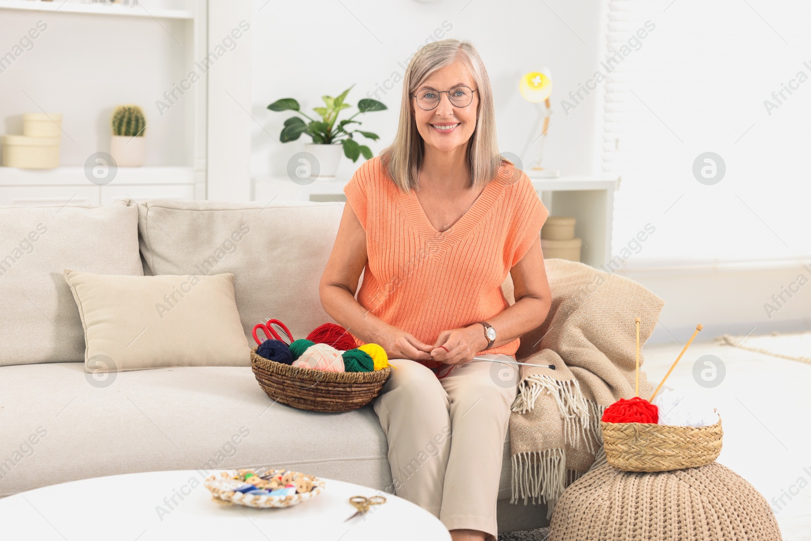 Photo of Smiling senior woman with skeins of yarn on sofa at home