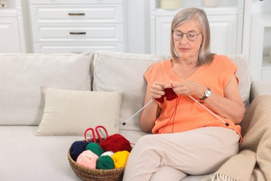 Beautiful senior woman knitting on sofa at home