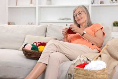 Beautiful senior woman knitting on sofa at home