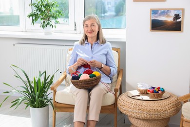 Beautiful senior woman knitting on armchair at home