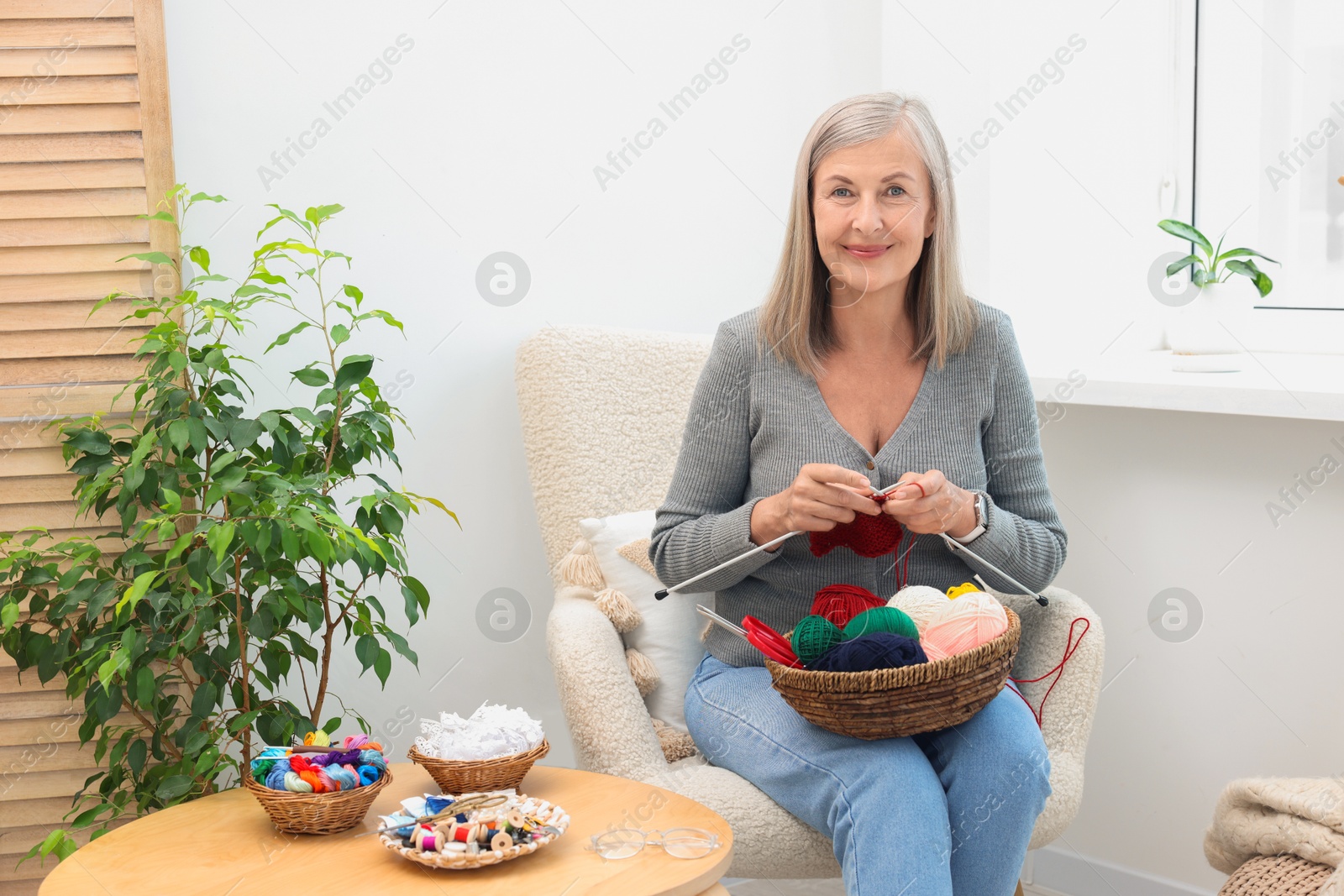 Photo of Beautiful senior woman knitting on armchair at home