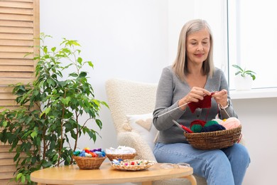 Photo of Beautiful senior woman knitting on armchair at home