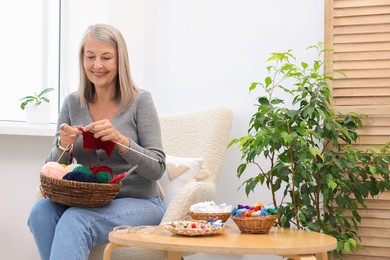 Photo of Smiling senior woman knitting on armchair at home