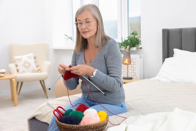 Beautiful senior woman knitting on bed at home