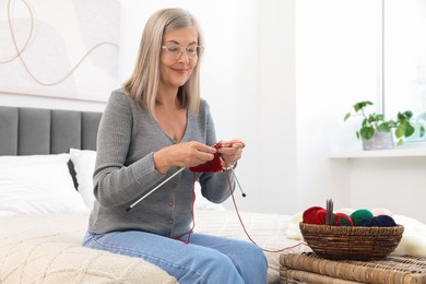 Photo of Beautiful senior woman knitting on bed at home