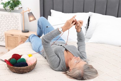 Beautiful senior woman knitting on bed at home