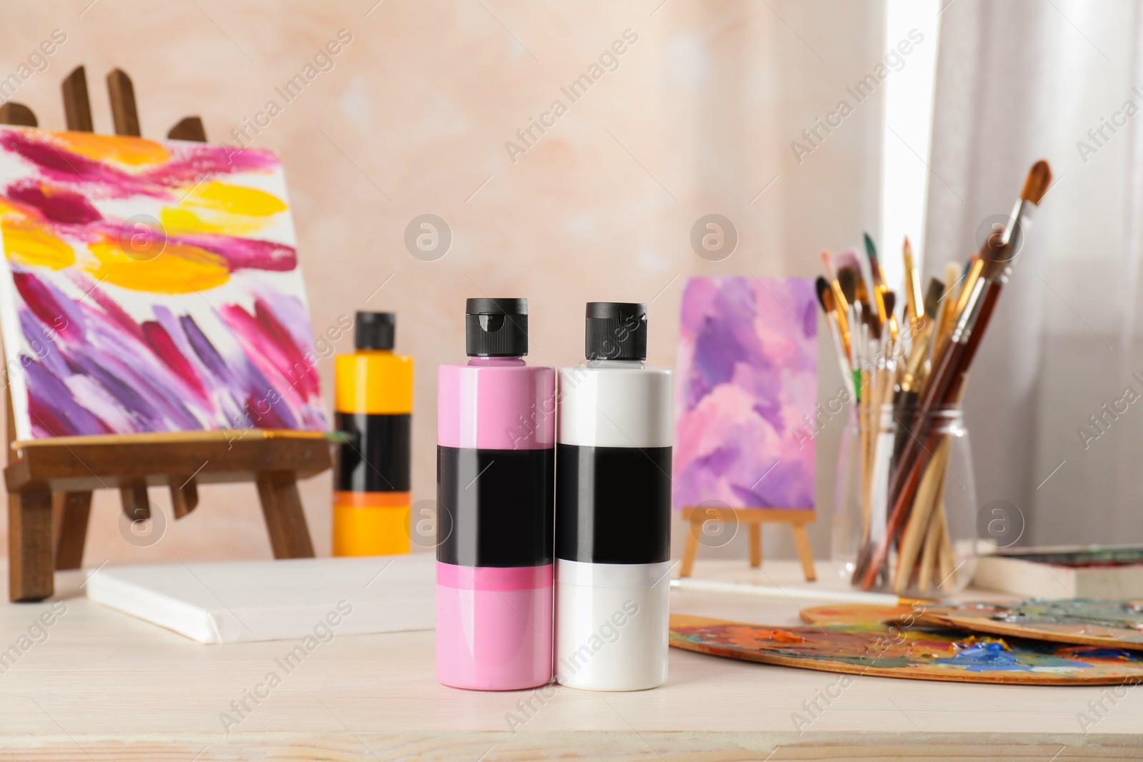 Photo of Acrylic paints of different colors, small easel, palette and brushes on wooden table indoors