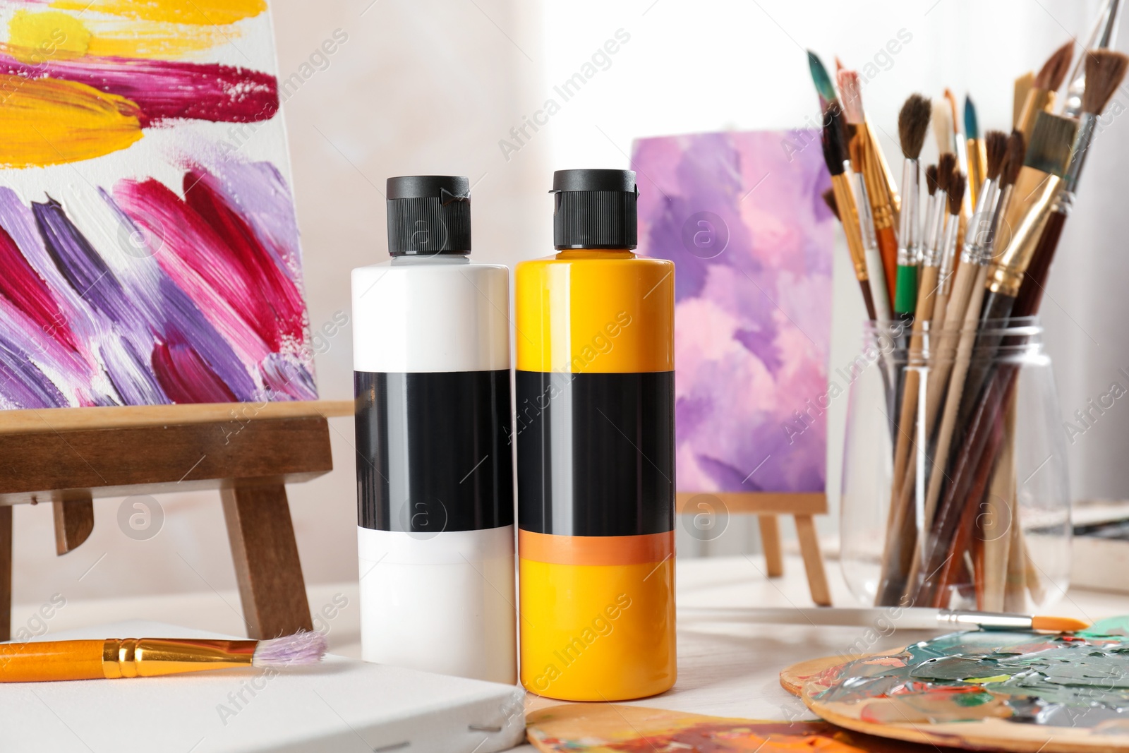 Photo of Acrylic paints of different colors, small easels, palettes and brushes on light table indoors