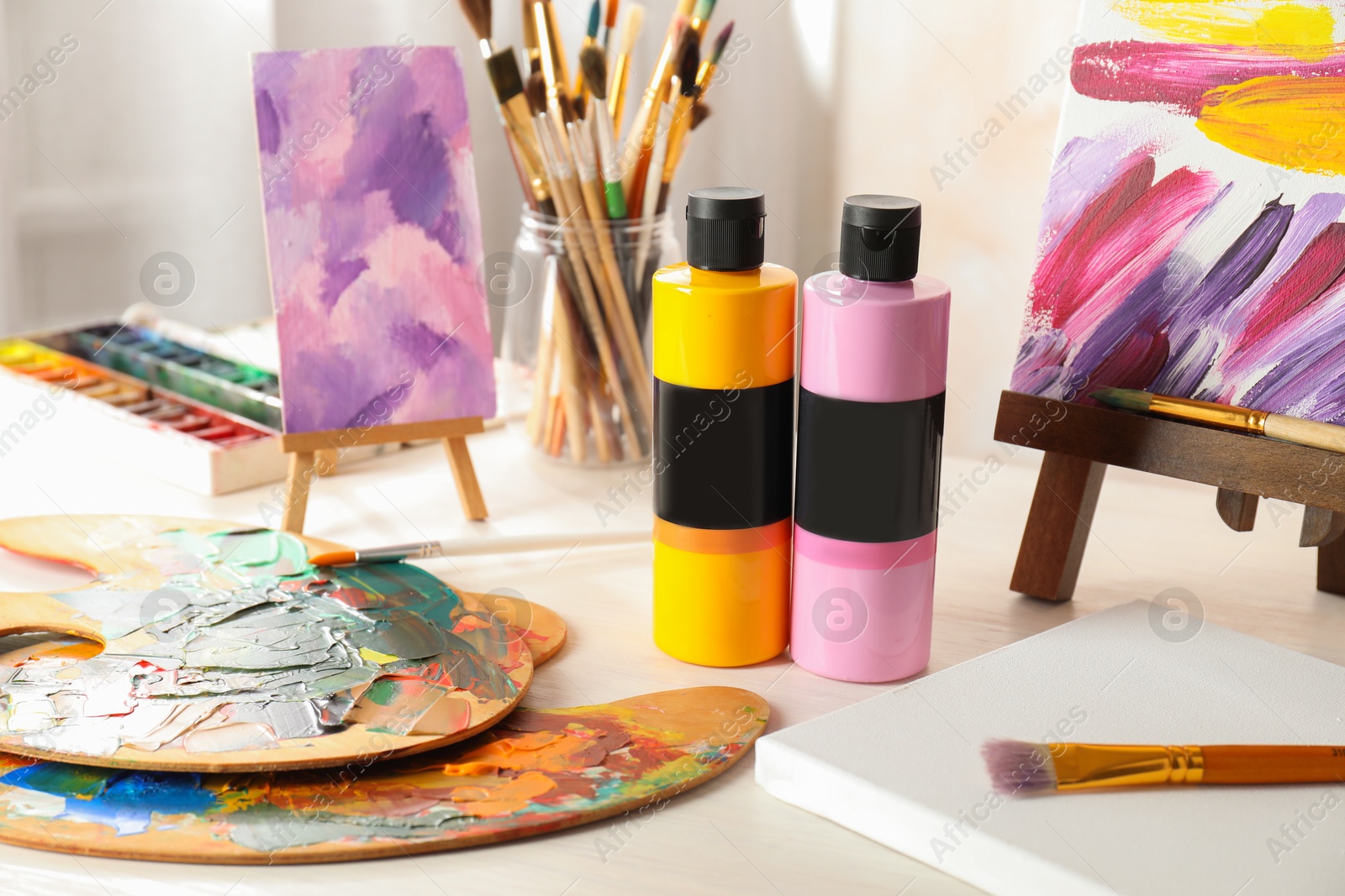 Photo of Acrylic paints of different colors, small easels, palettes and brushes on wooden table indoors