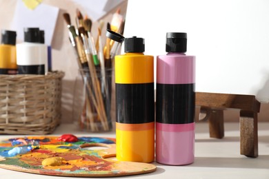 Photo of Acrylic paints of different colors, palette, small easel and brushes on wooden table