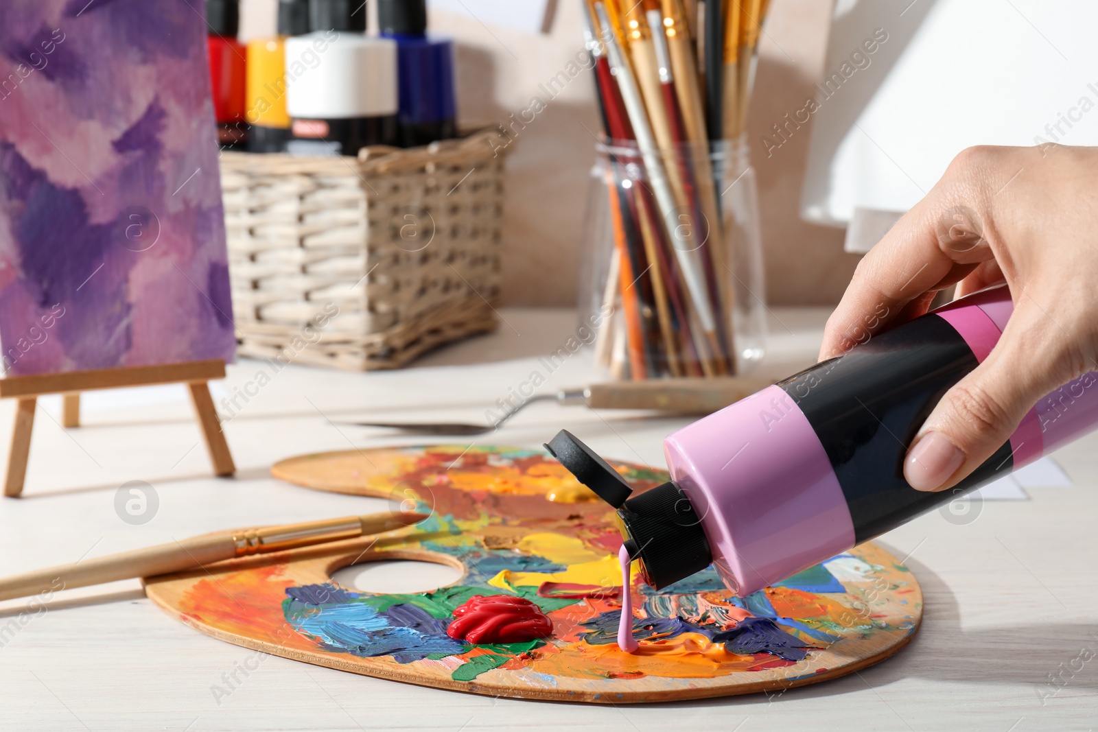 Photo of Woman mixing paints on palette at wooden table indoors, closeup