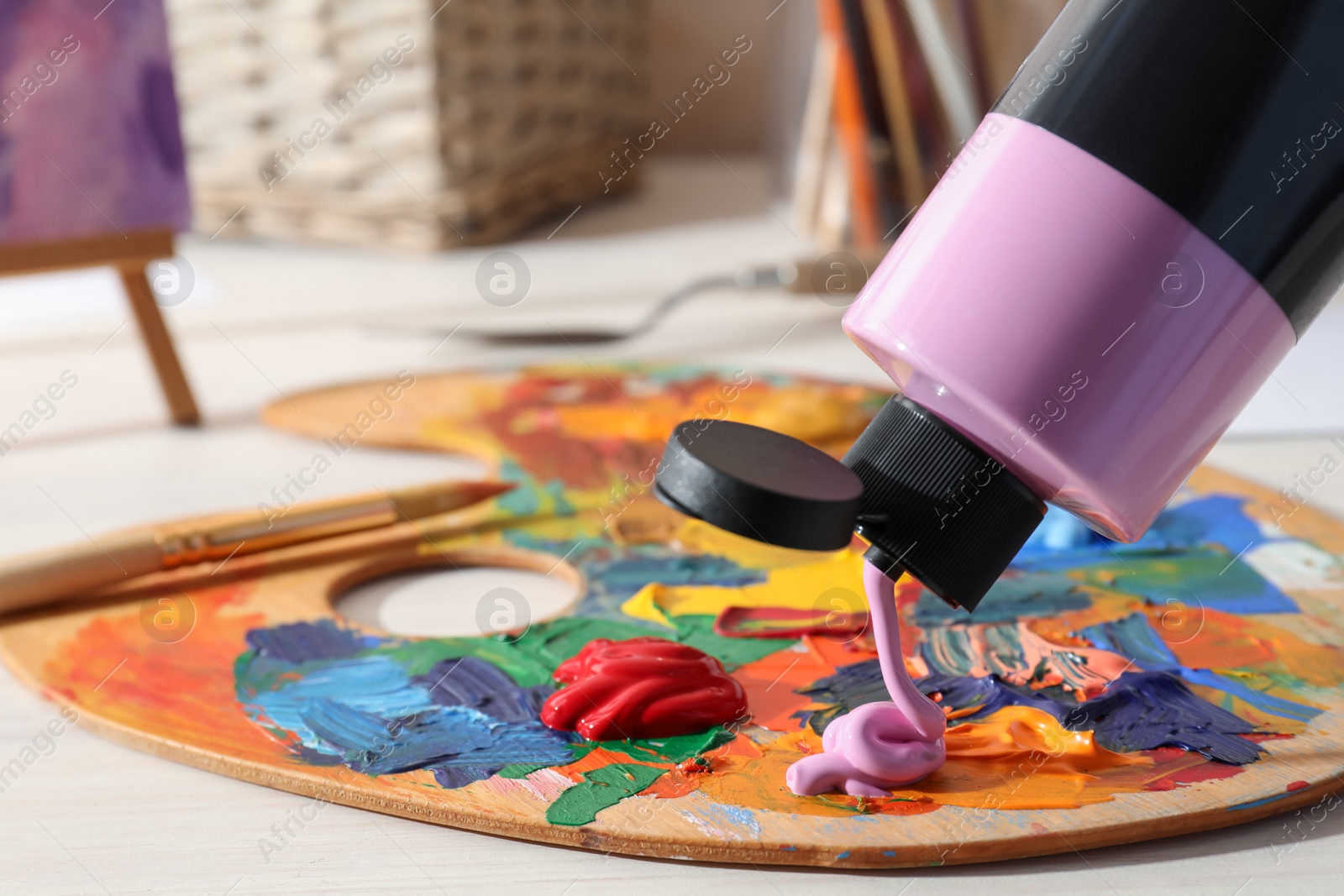 Photo of Squeezing violet acrylic paint on palette at wooden table indoors, closeup