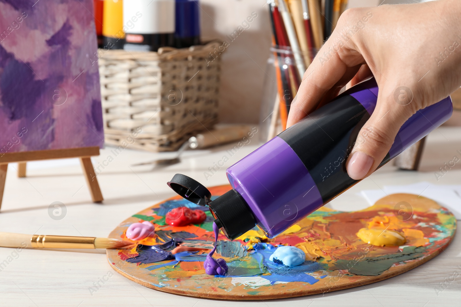 Photo of Woman mixing paints on palette at wooden table indoors, closeup