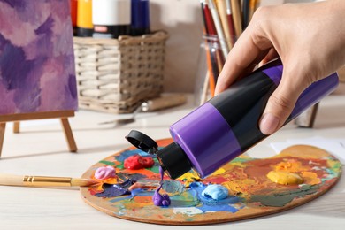 Photo of Woman mixing paints on palette at wooden table indoors, closeup