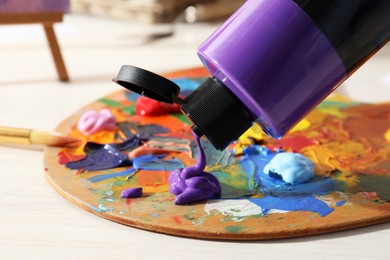 Photo of Squeezing purple acrylic paint on palette at wooden table indoors, closeup