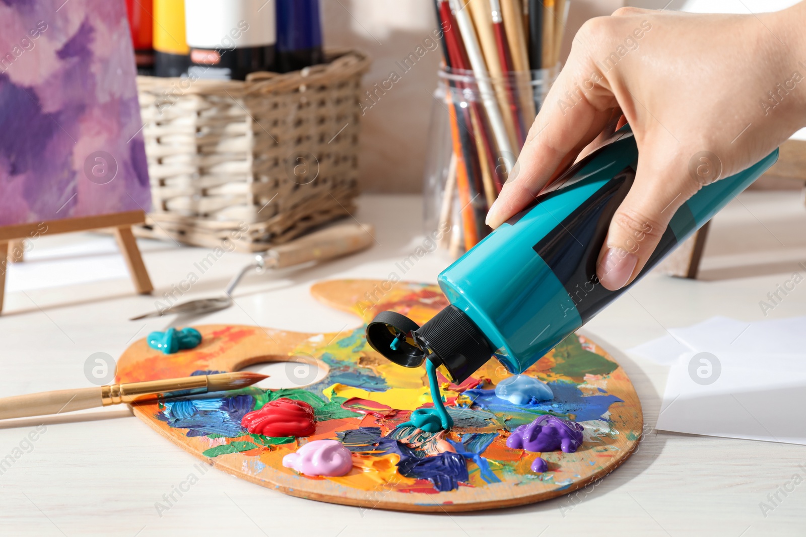 Photo of Woman mixing paints on palette at wooden table indoors, closeup