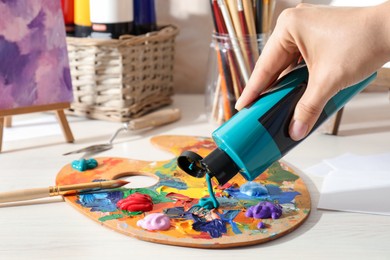 Photo of Woman mixing paints on palette at wooden table indoors, closeup