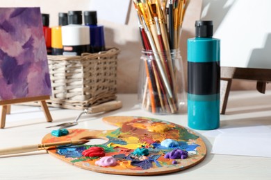 Artist's palette with mixed paints, brushes and small easels on wooden table