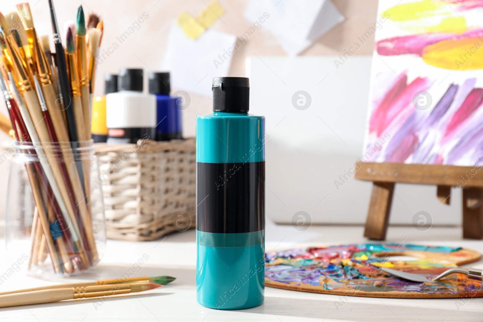 Photo of Turquoise acrylic paint in bottle, palette and brushes on wooden table indoors