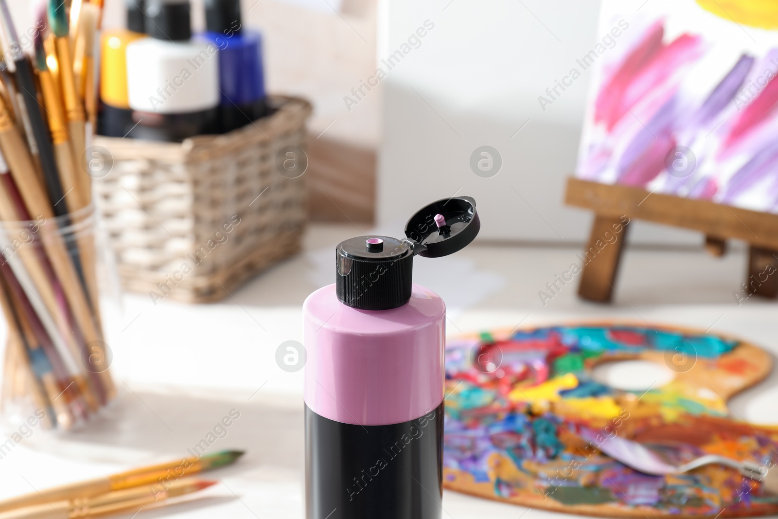 Photo of Pink acrylic paint in bottle, palette and brushes on table indoors