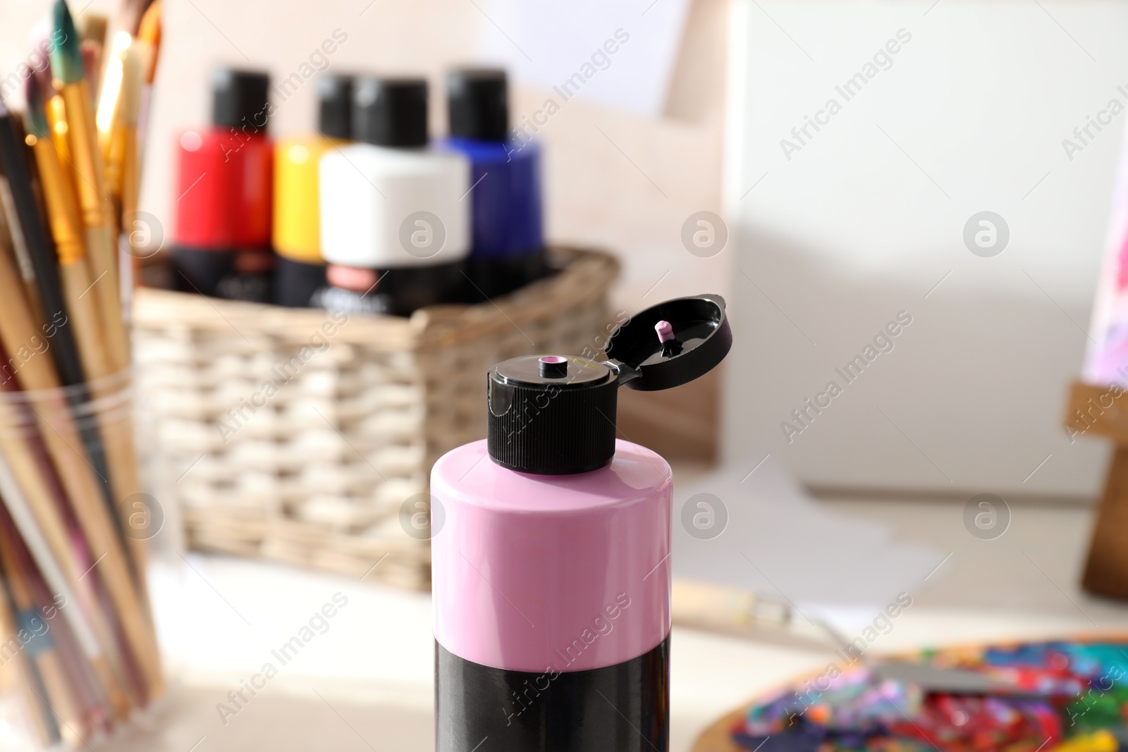 Photo of Pink acrylic paint in bottle, palette and brushes on table indoors, closeup