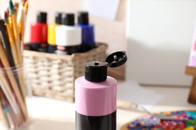 Photo of Pink acrylic paint in bottle, palette and brushes on table indoors, closeup