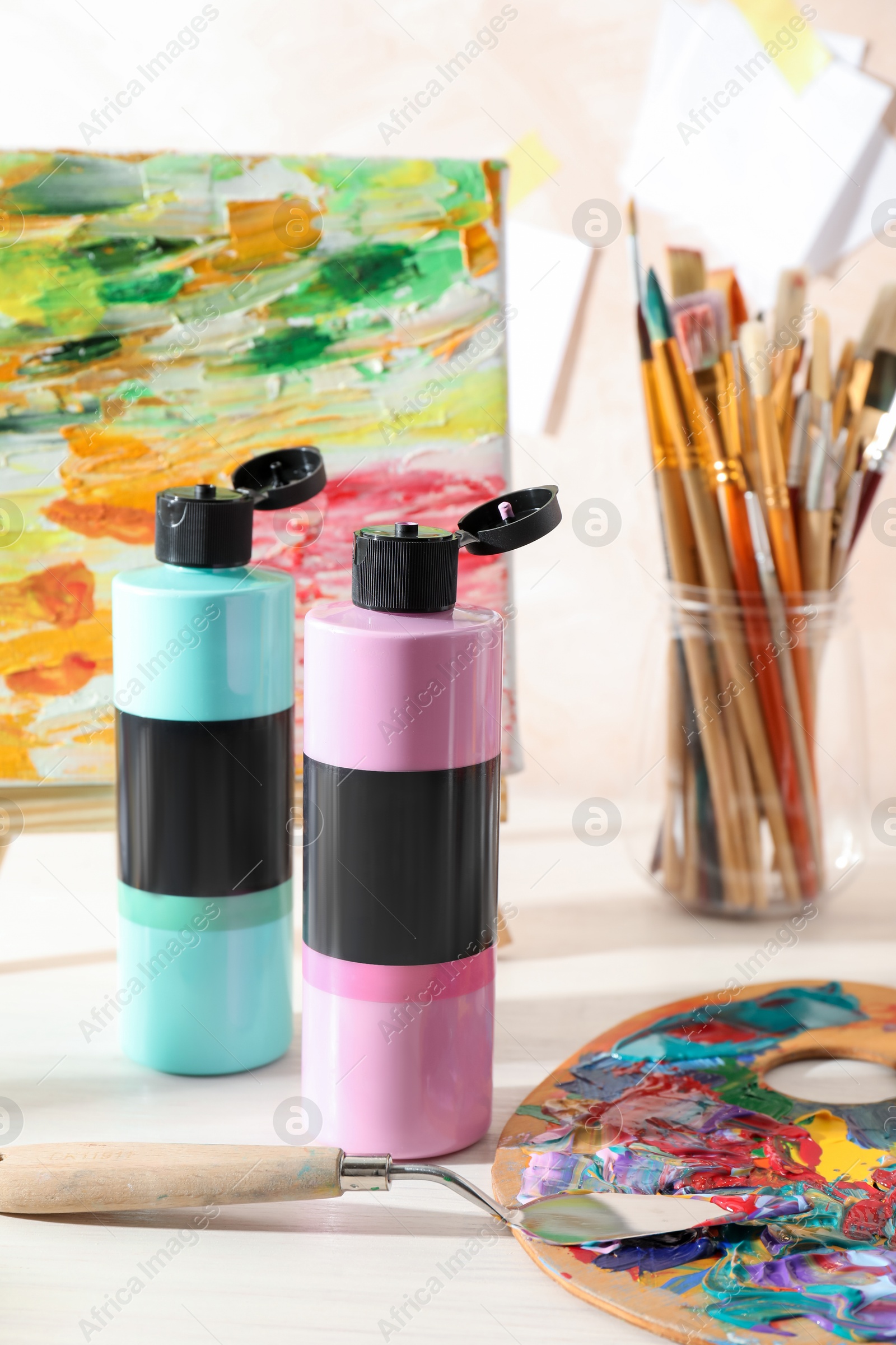 Photo of Acrylic paints of different colors, palette, knife, brushes and small easel with abstract picture on wooden table