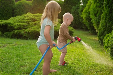 Photo of Little boy and his sister watering lawn with hose in backyard