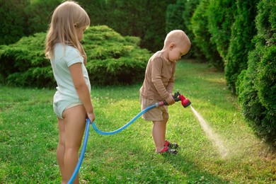 Little boy and his sister watering lawn with hose in backyard