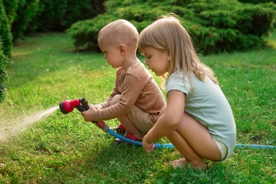 Little boy and his sister watering lawn with hose in backyard